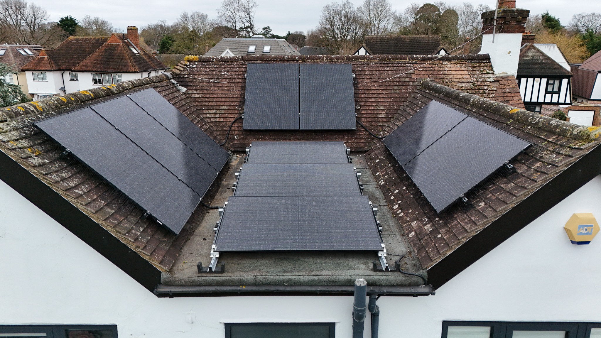 Solar panels across pitched and flat sections of a roof, photographed by drone